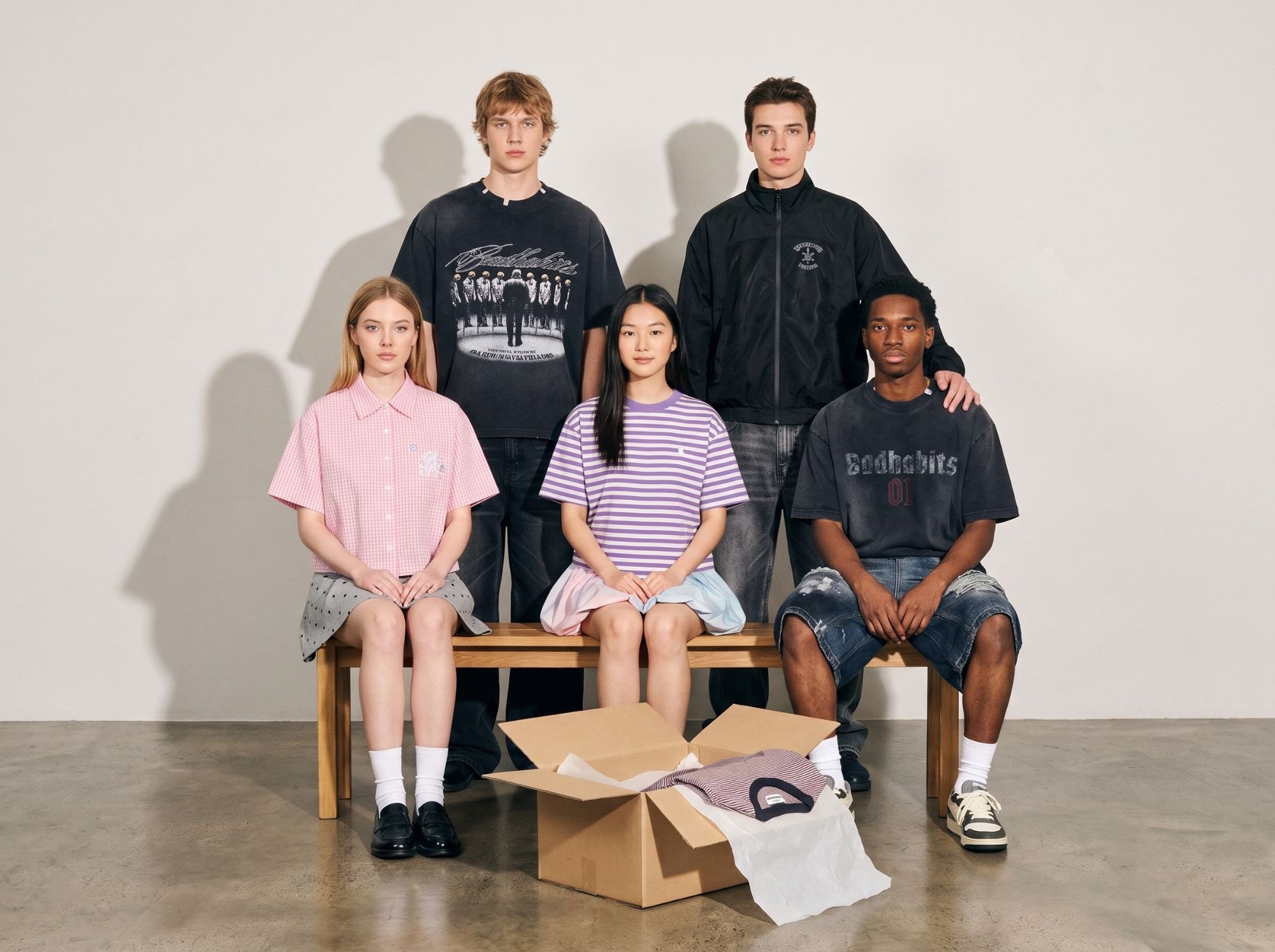 Fünf Freunde in Bad Habits und Bad Rabbit, formell aufgestellt wie auf einem Klassenfoto, vor ihnen ein offenes Paket